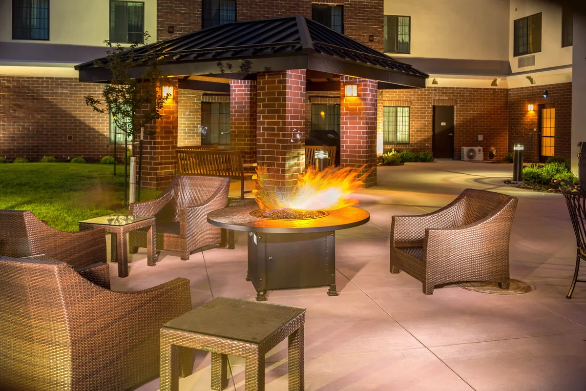 An exterior communal area featuring a fire pit surrounded by woven chairs and supported by brick columns. The setting is ideal for socializing, relaxing, and enjoying the outdoors—particularly suited to evening gatherings and cookouts.