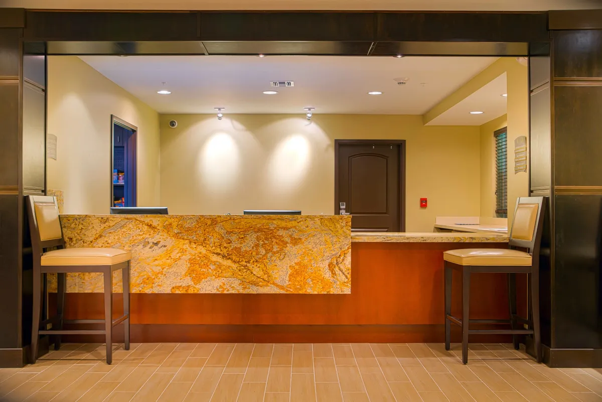 A welcoming reception area with a granite-top desk, two bar stools, and decorative wall paneling. The space is warm and inviting, hinting at attentive guest services and a positive first impression upon arrival.