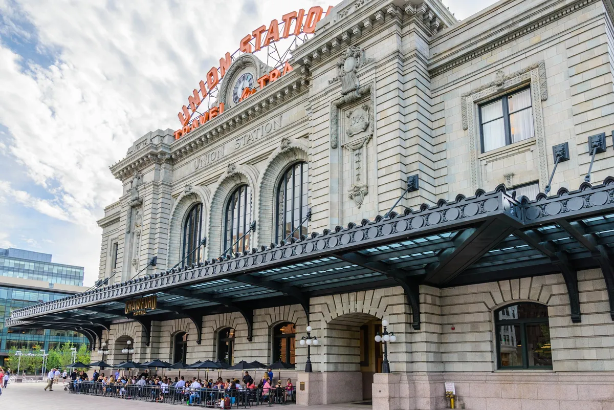 This image showcases the historical architecture of Denver's Union Station, complete with a large clock and its iconic neon sign. The outdoor seating area is lively, suggesting a vibrant urban transit hub that connects travelers to the city's business districts.