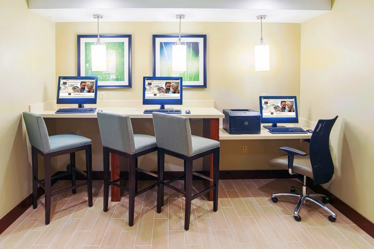 A stylish business center with computers, bar stools, a printer, and framed artwork. The space is inviting and functional, supporting productivity for business travelers and guests who need to work remotely or print documents.
