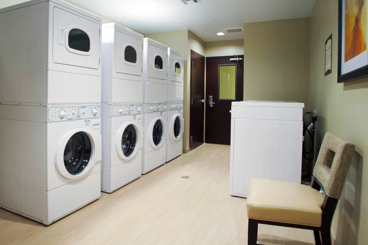A functional laundry area equipped with stacked washers and dryers, a single washing machine, and a simple chair for waiting. The space is clean and straightforward, making it easy for guests to complete laundry tasks during extended stays.