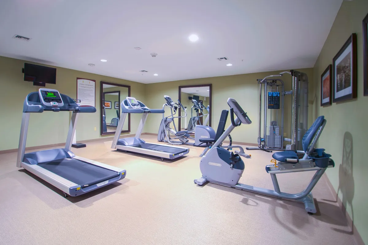 A well-equipped fitness center featuring treadmills, elliptical machines, a recumbent bike, and strength training equipment. The room is bright, airy, and designed for both individual workouts and group fitness sessions, promoting an energetic atmosphere.
