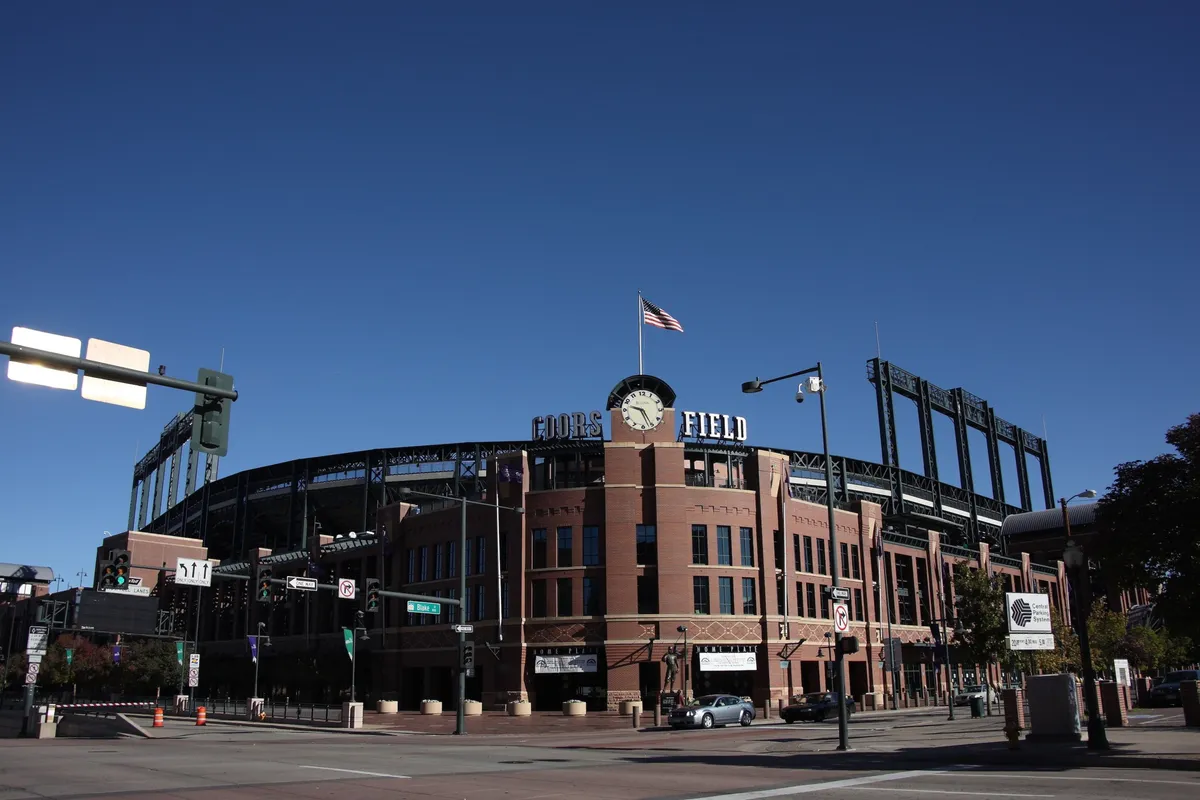 This photo showcases the recognizable Coors Field sign against a backdrop of brick architecture, with the American flag flying and the stadium’s structure visible. The image evokes the community spirit of attending a baseball game, tailgating, or joining local festivities, connecting viewers with the city’s sports culture and neighborhood energy.