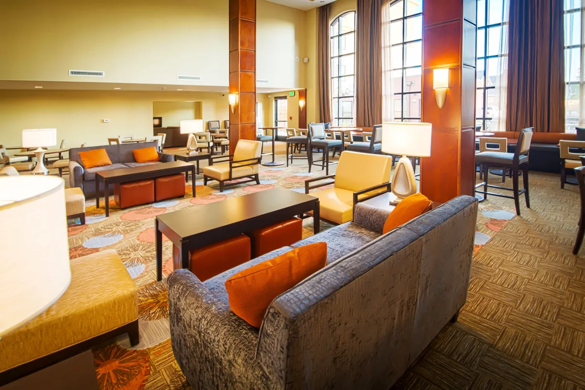 A spacious living area featuring large windows that let in natural light, comfortable seating options, and decorative lighting fixtures. The room feels open yet cozy, ideal for gathering, relaxing, or catching up on entertainment.